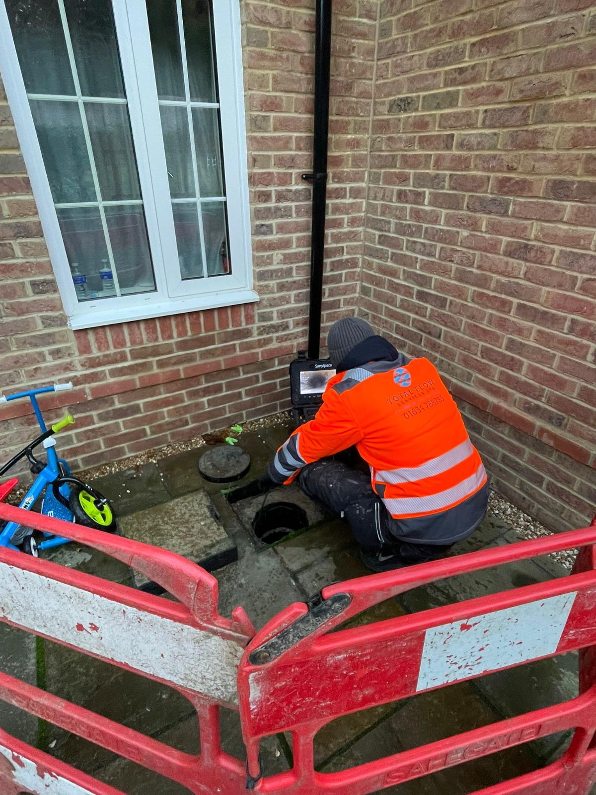 Engineer inspecting an open inspection chamber on patio paving before installing a patch liner — Kent property